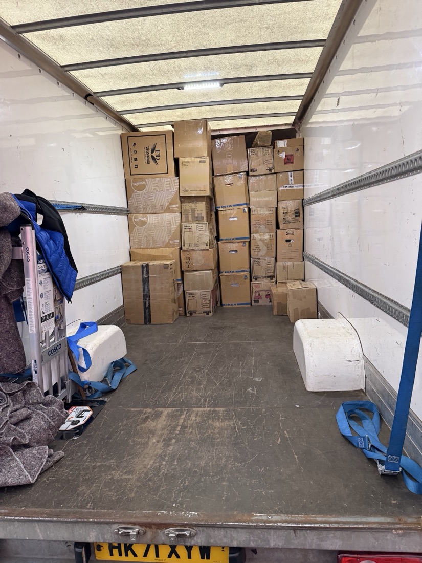 Inside the Luton van, moving boxes stacked square against the bulkhead with straps ready